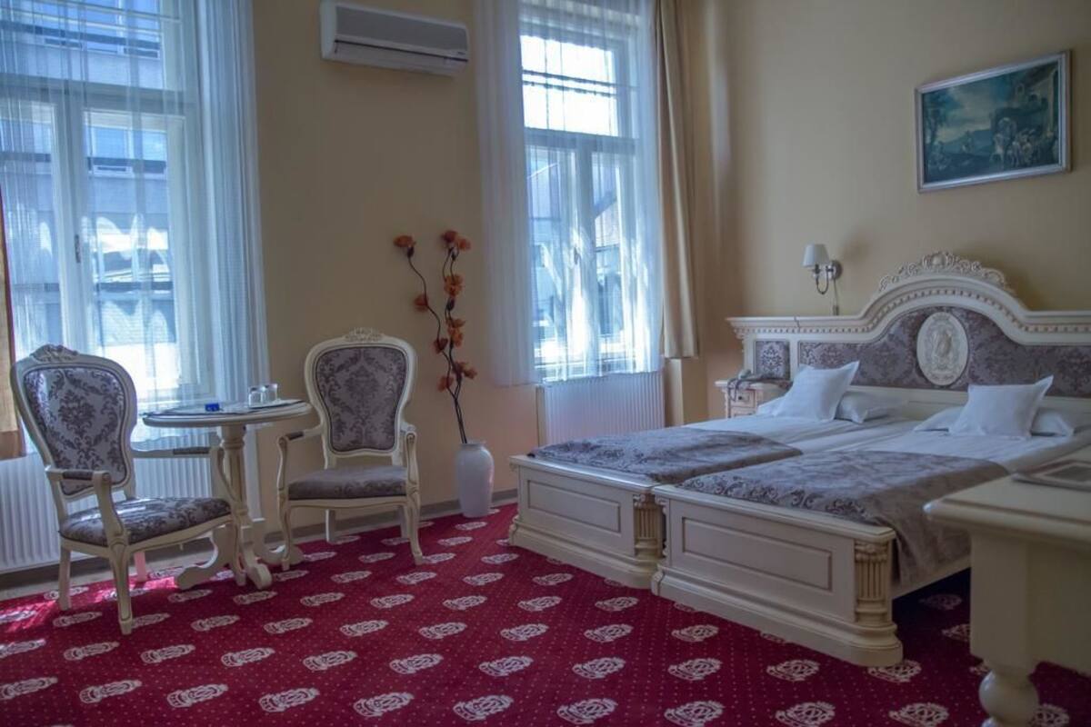 A hotel room with a large bed, two bedside tables, a chair, a small table, and a vase with flowers.