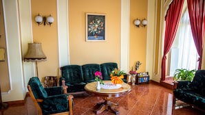 A living room with a green sofa set, a round coffee table with flowers, and a painting on the wall. - Hotel Astoria (Satu Mare)