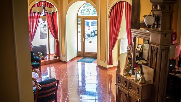 A hotel lobby with a tiled floor, red curtains, a reception desk, and a chandelier. - Hotel Astoria (Satu Mare)
