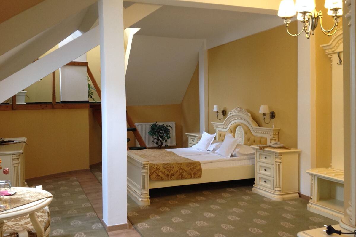 A bedroom with a bed, nightstands, a dresser, a chandelier, and a staircase.