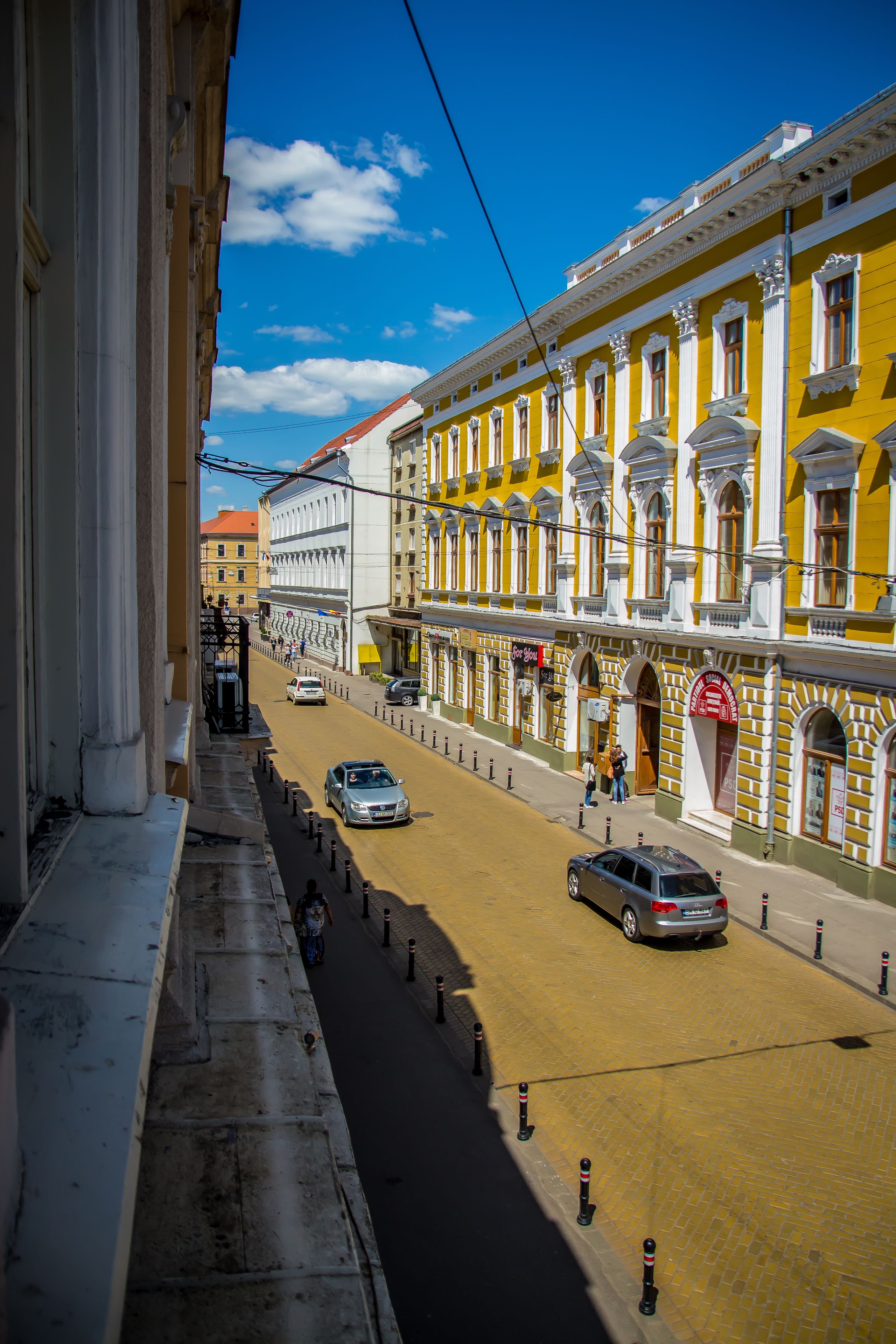 A street view with yellow buildings, a clear sky, and a few cars on the road.