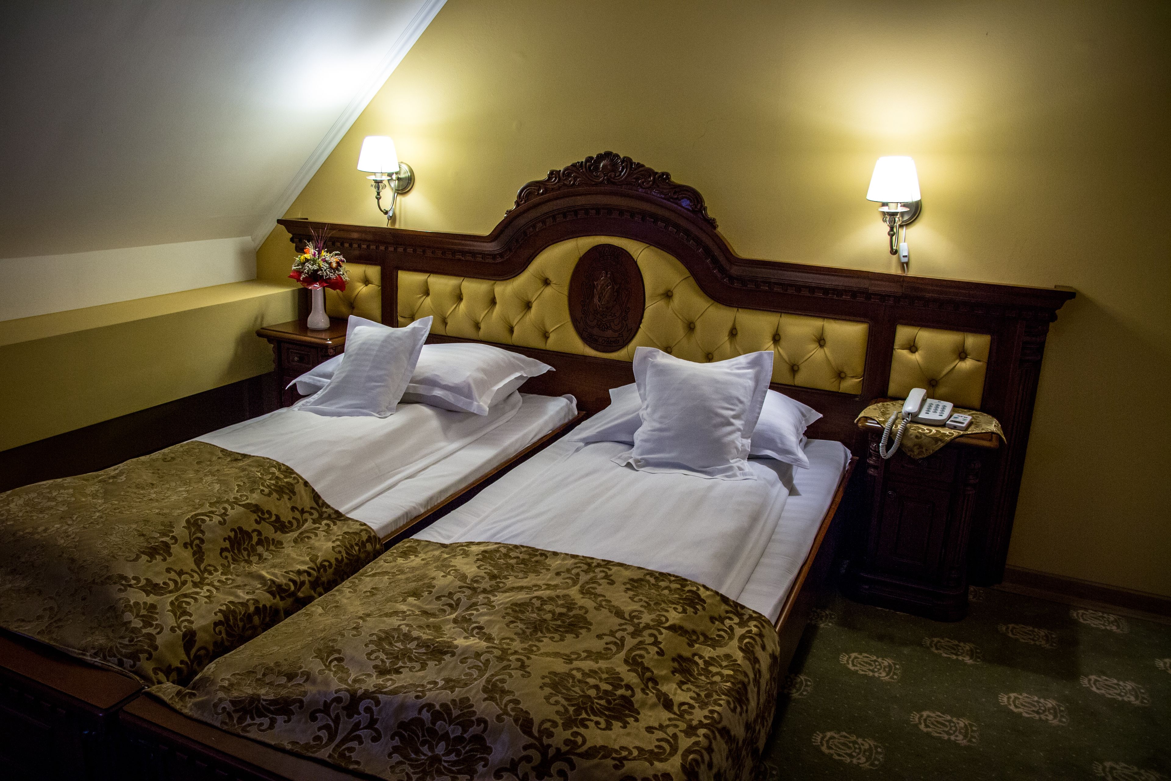 A hotel room with two beds, a wooden headboard, bedside lamps, a telephone, and a vase with flowers.