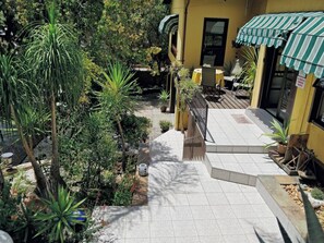 A courtyard with a tiled pathway leading to a building with a green-striped awning. - Maison Ambre Guesthouse (Windhoek)