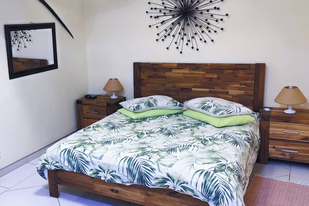 A bedroom with a wooden bed, two nightstands, a wall clock, a mirror, and a tropical-themed bedspread.