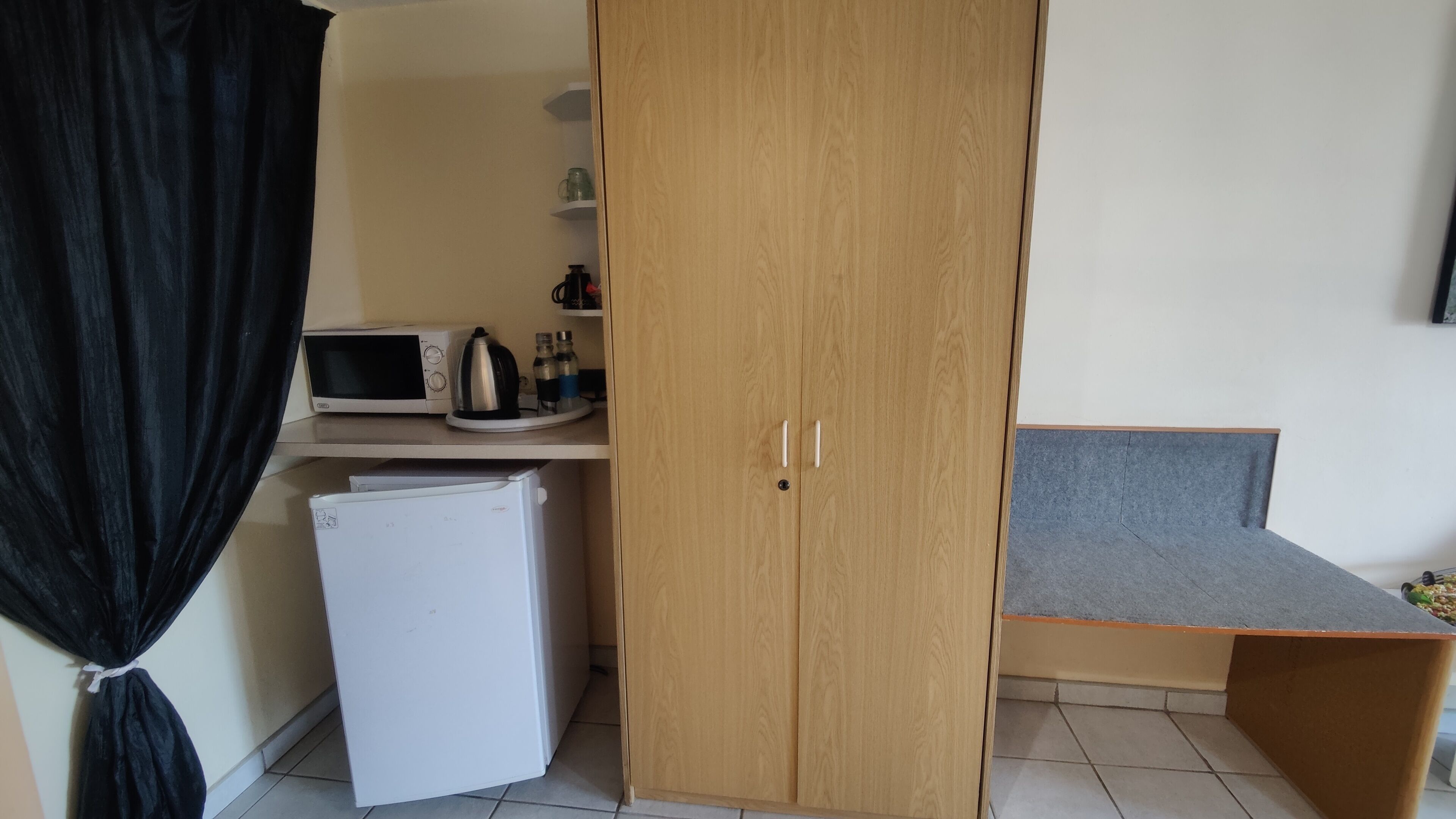 A compact kitchenette with a microwave, kettle, and refrigerator.