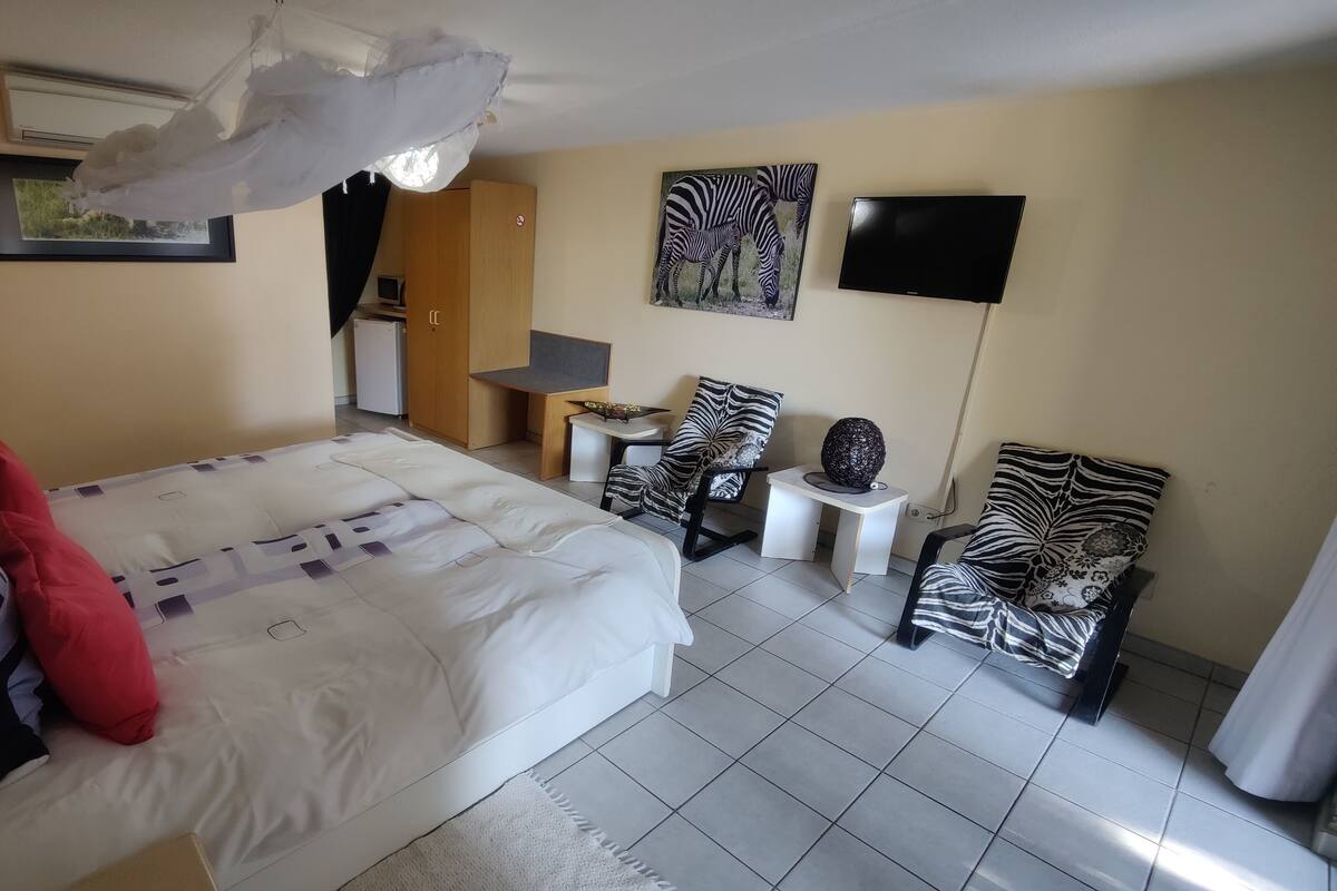A hotel room with a bed, two chairs, a small table, a TV, and a zebra-themed painting.
