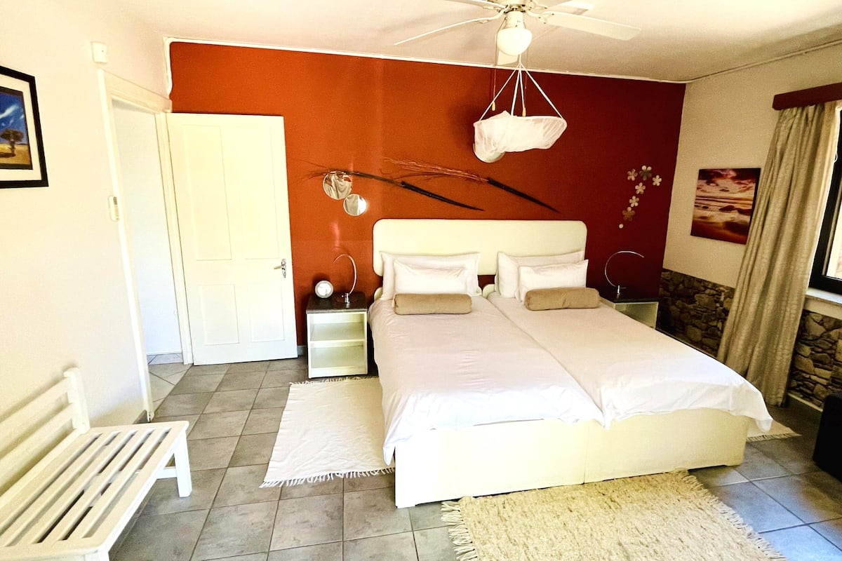 A bedroom with a bed, a ceiling fan, a nightstand, a bench, and a door.
