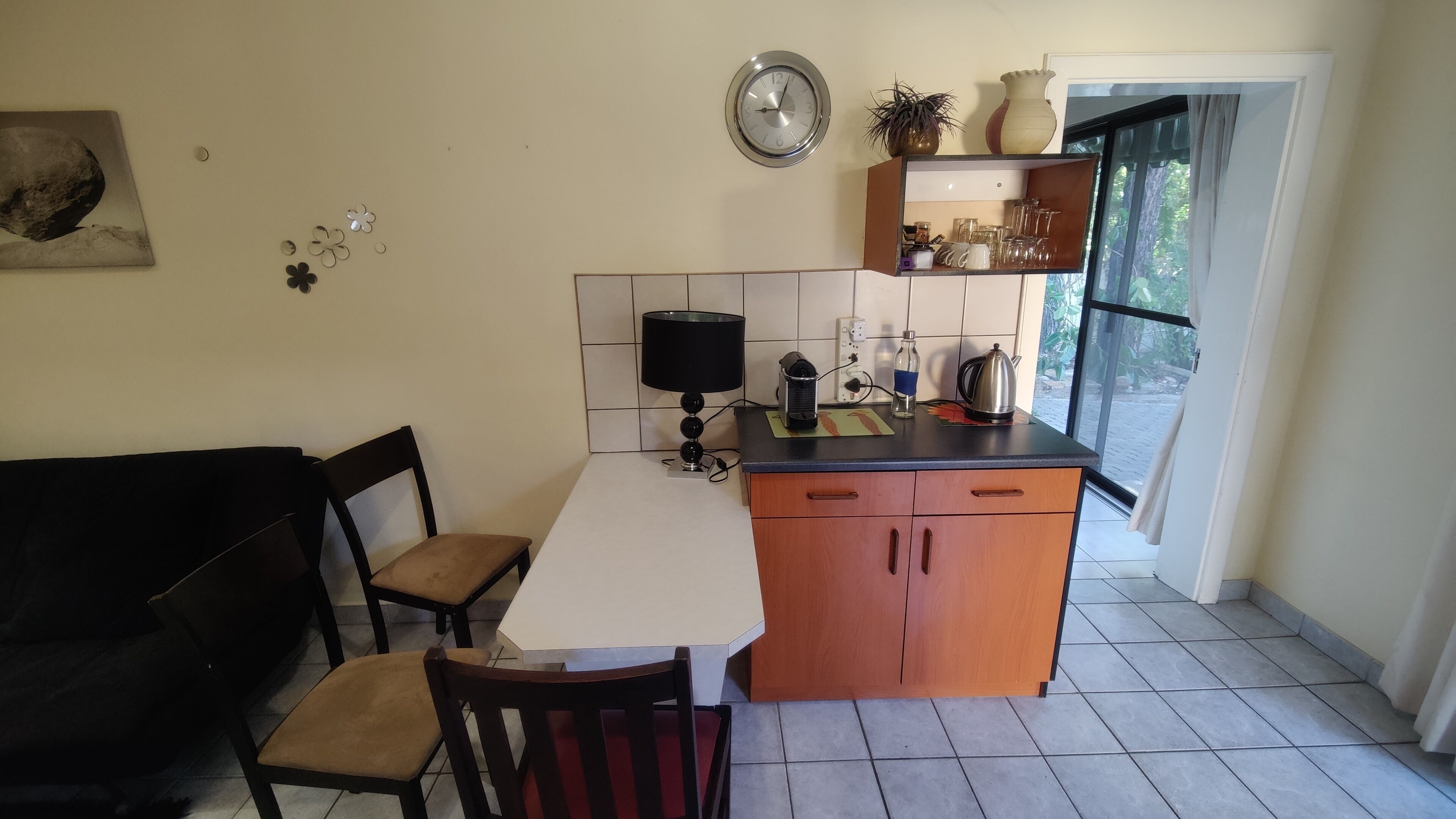 Una cocina compacta con comedor, que cuenta con una pequeña isla, un reloj en la pared y una ventana con vista a la vegetación.
