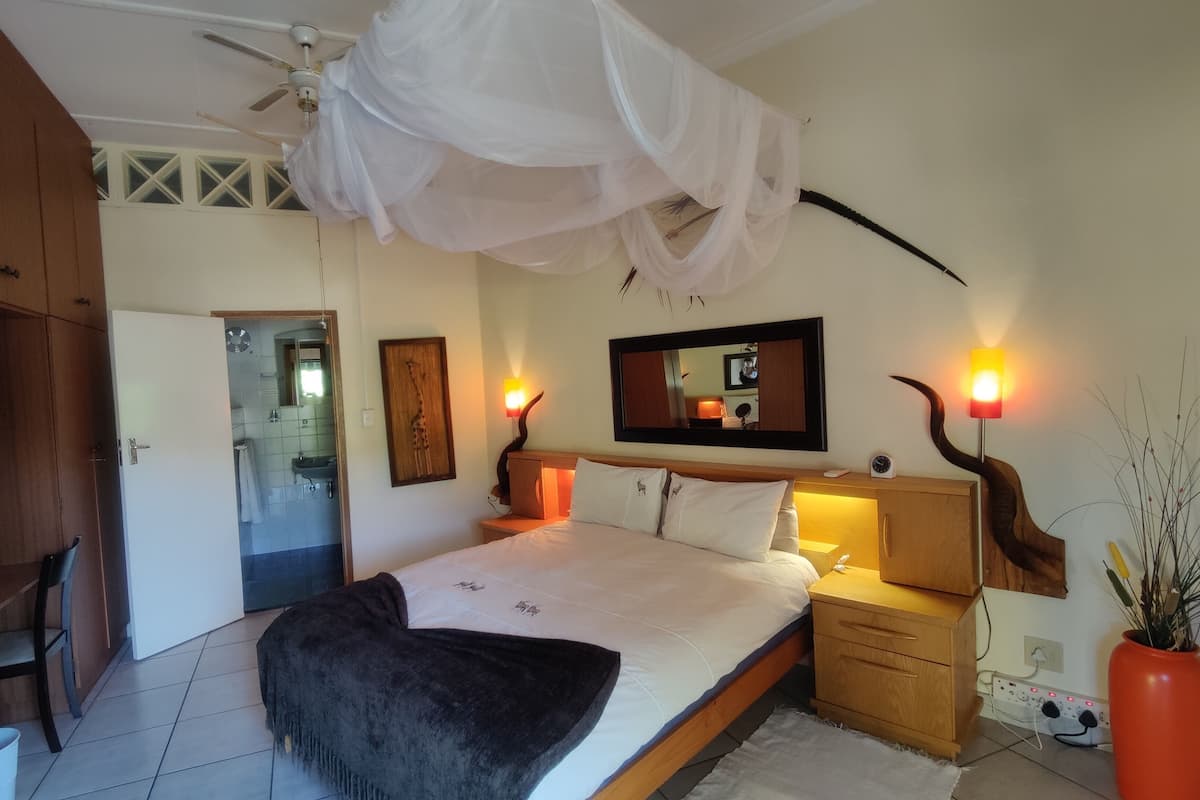 A bedroom with a bed, bedside lamps, a nightstand, a wooden wardrobe, a ceiling fan, and a large mirror.