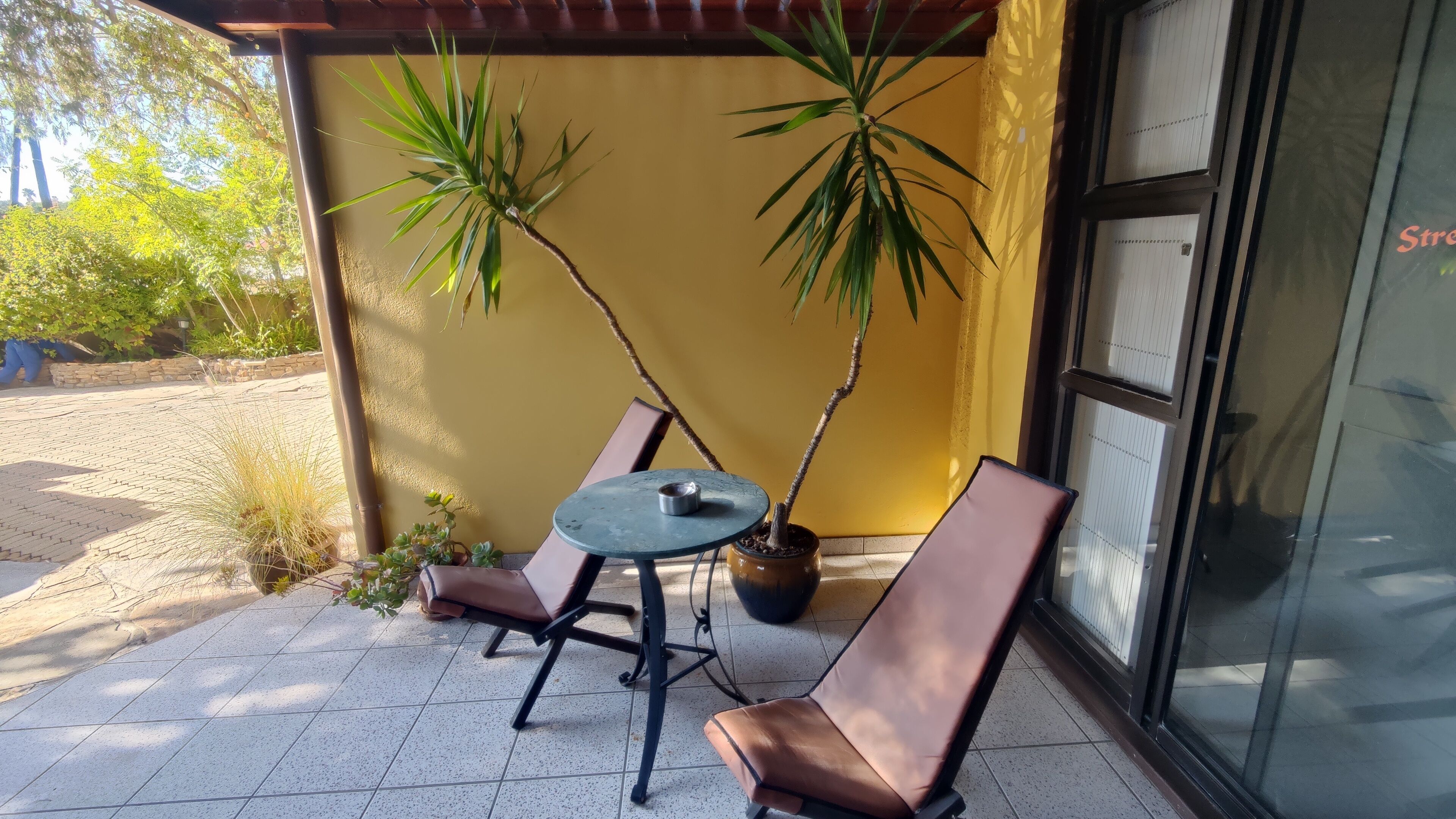 Un patio con dos sillas, una mesa, una planta en maceta y una pared amarilla.