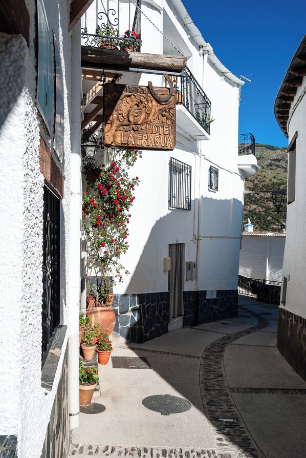 A narrow street with a white building featuring a wooden sign for 'Hotel La Faguas'. - Hotel La Fragua I (Trevelez)