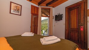 A hotel room with a bed, a TV mounted on the wall, and a balcony with a view of the countryside. - Hotel La Fragua I (Trevelez)