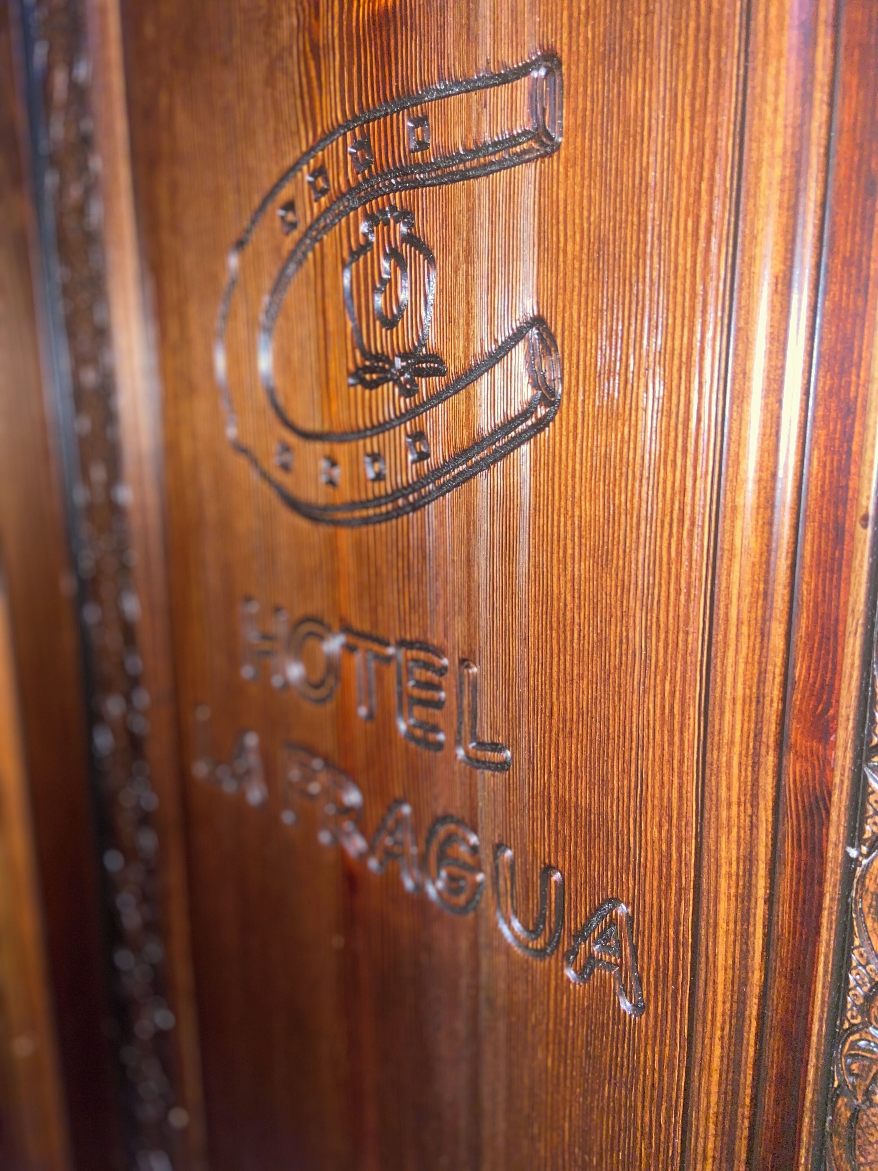Una puerta de madera con un logotipo en relieve y el texto "HOTEL PRAGU".