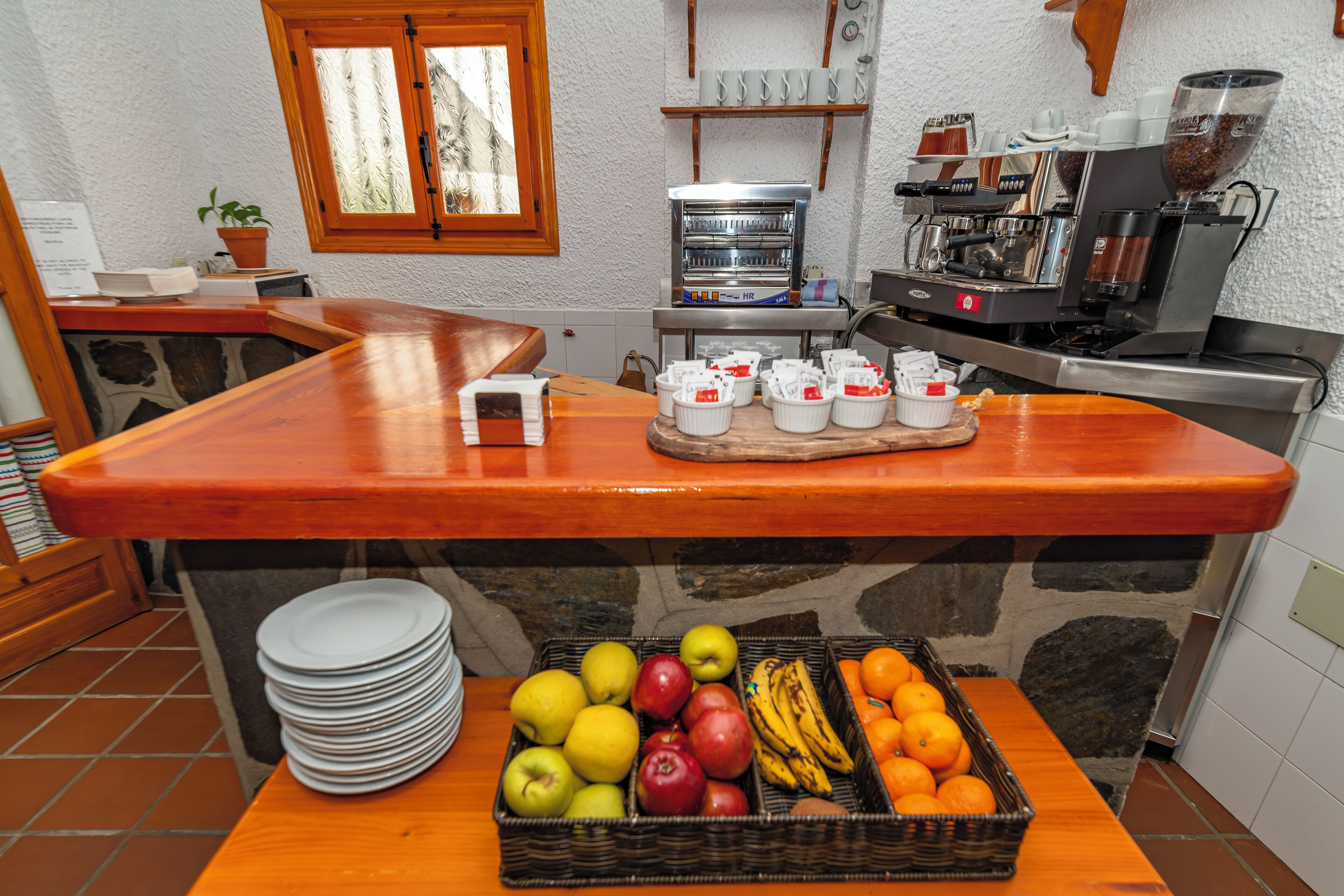 Uma área de cozinha com bancada de madeira, máquina de café e cesta de frutas.
