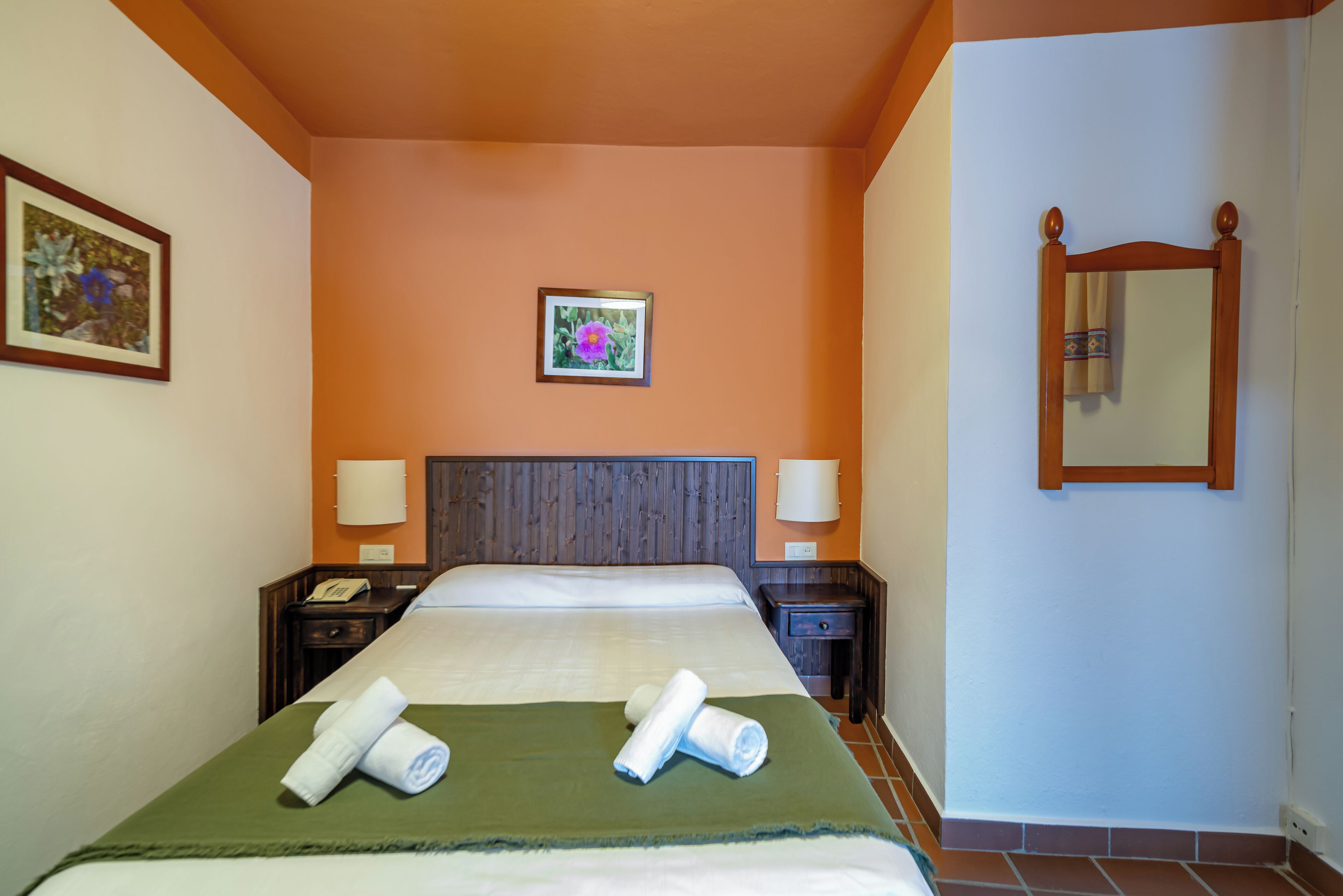 A hotel room with a large bed, two bedside tables, a nightstand, a framed picture on the wall, and a mirror.