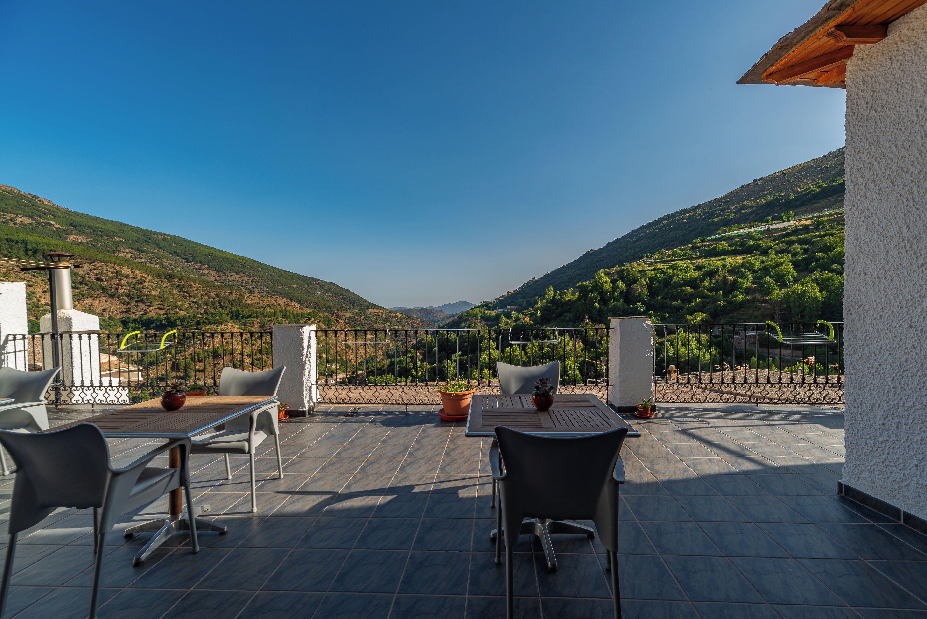 A terrace with a table and chairs, a potted plant, and a view of a valley.