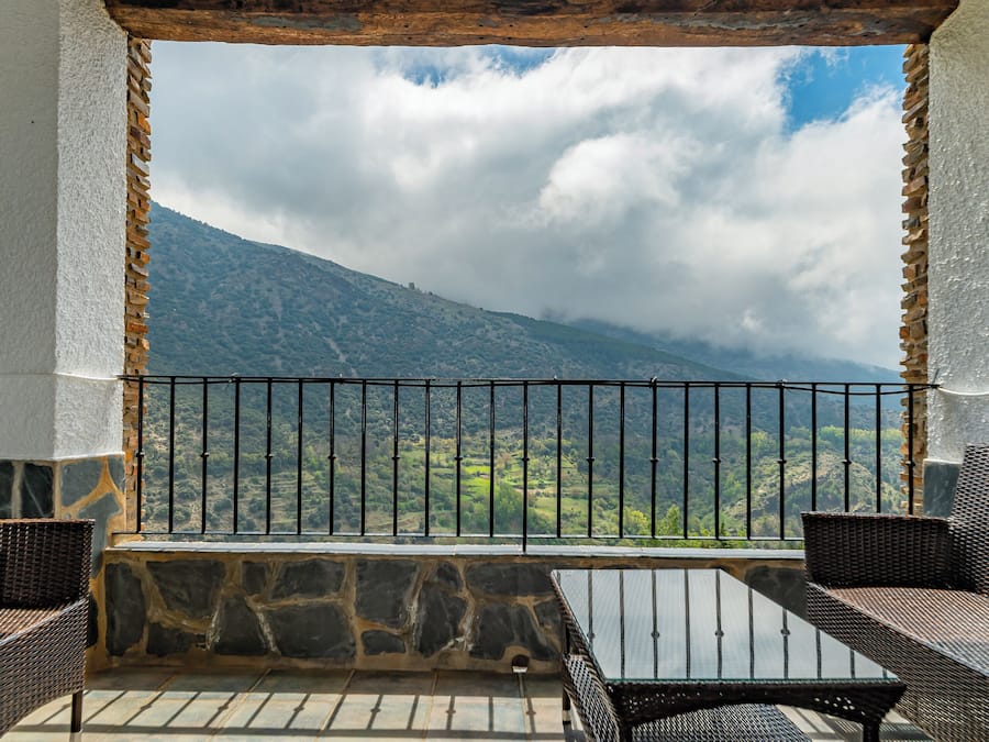 A balcony with stone walls, wooden beams, and wicker furniture.