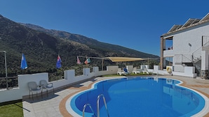 A swimming pool with a view of mountains, a covered area with chairs, and flags. - Hotel La Fragua II (Trevelez)