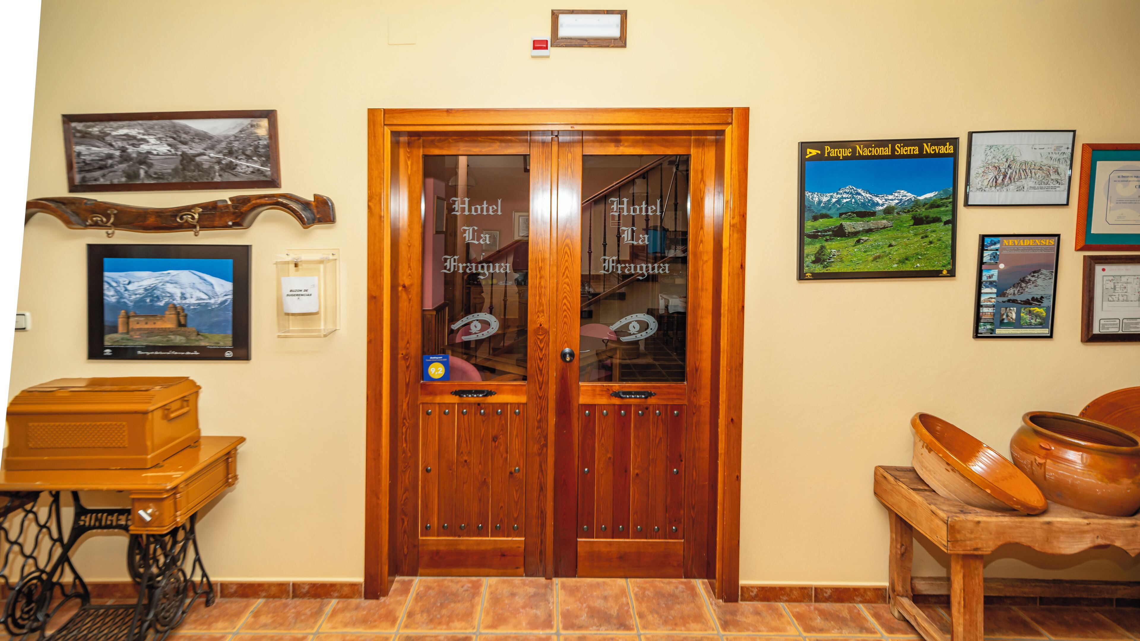 Una puerta doble de madera con el letrero 'Hotel La Fragua', piso de baldosas y varias fotografías enmarcadas en las paredes.