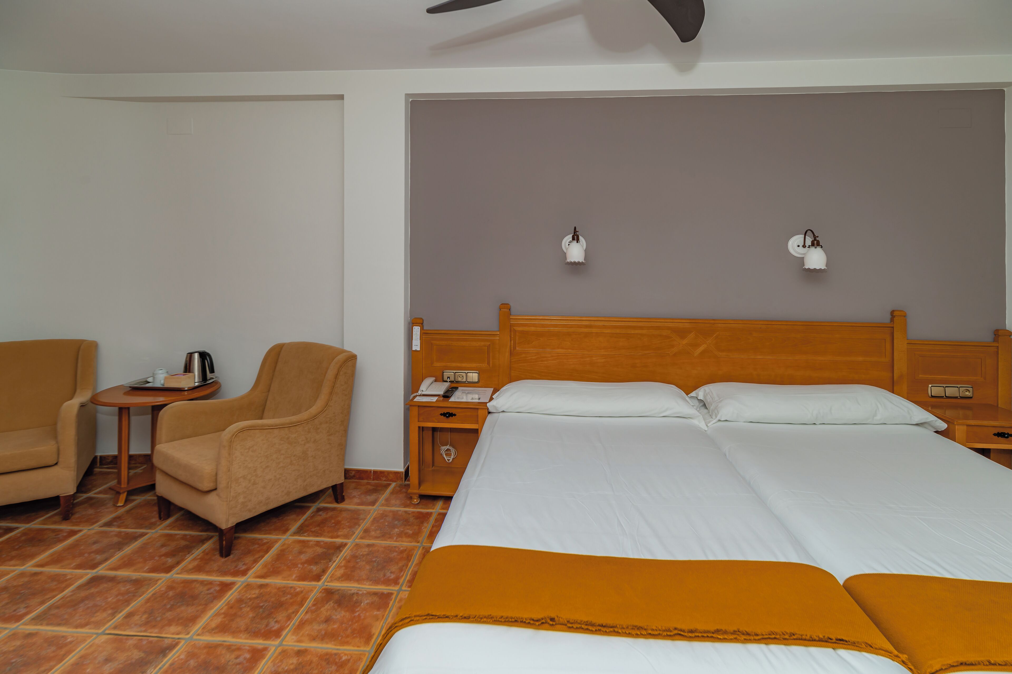Een hotelkamer met een groot bed, twee nachtkastjes, een stoel en een klein tafeltje met een waterkoker.