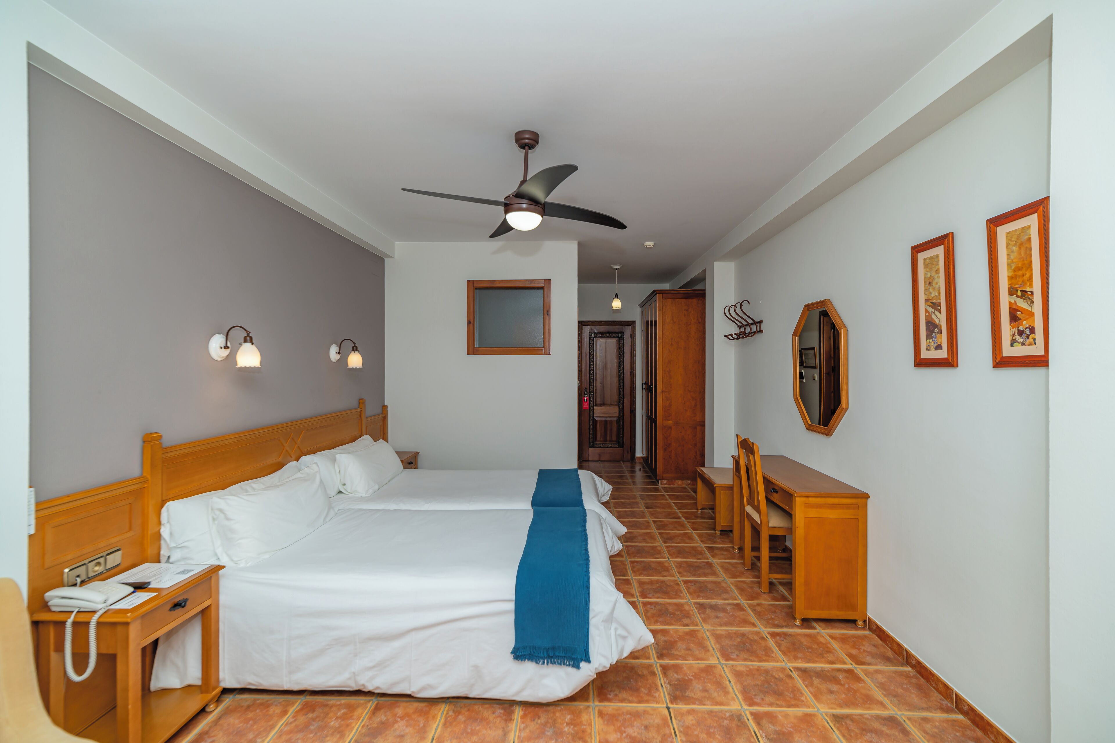 Habitación de hotel con dos camas, un escritorio, una silla, un teléfono, un espejo y un ventilador de techo.