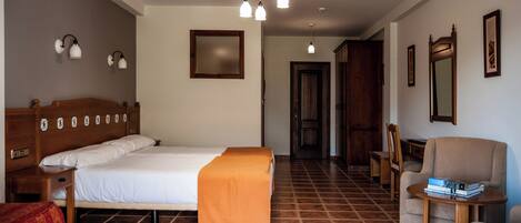 A hotel room with a large bed, a wooden headboard, a small table with a chair, and a mirror on the wall.