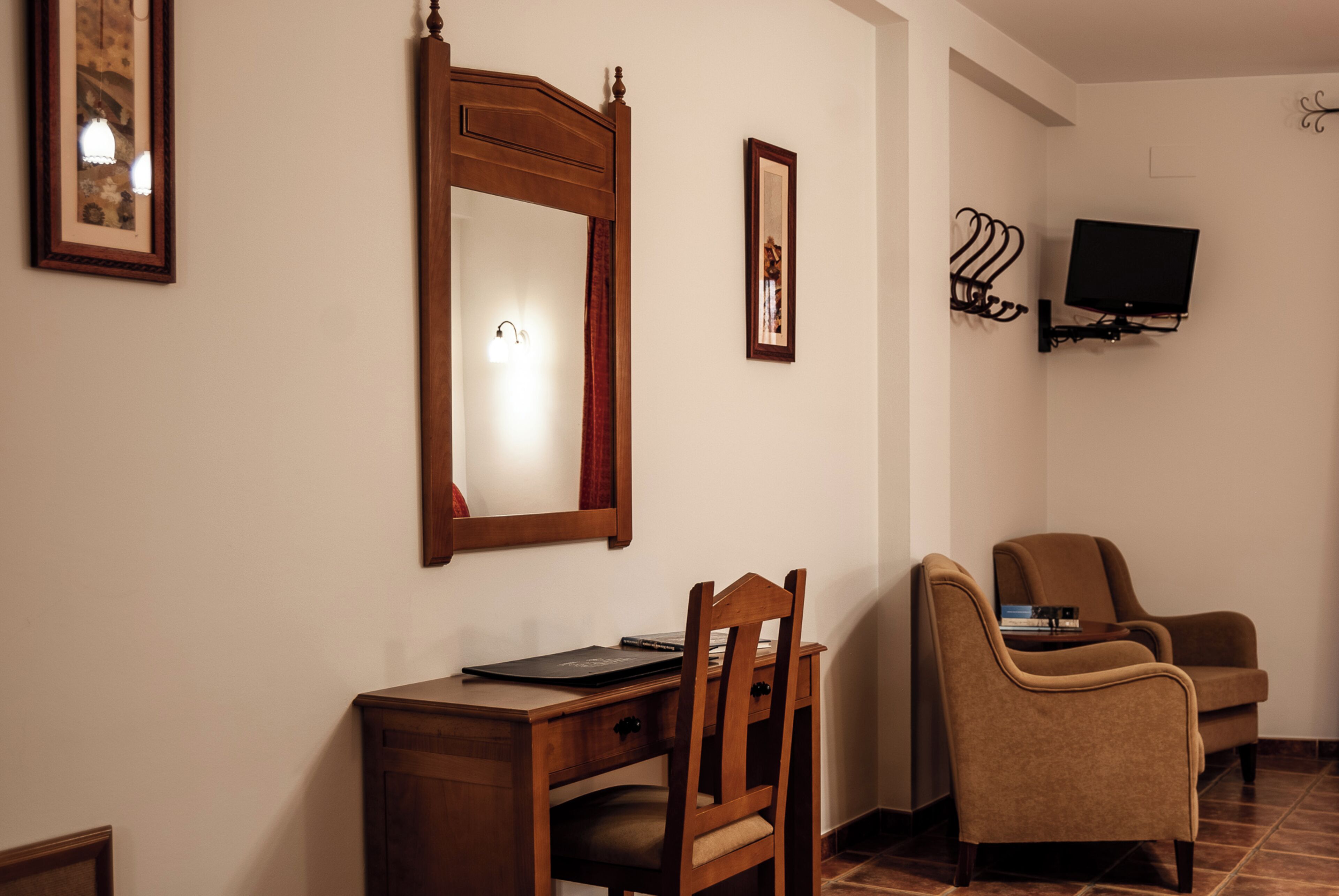 A hotel room with a wooden desk, a chair, a television mounted on the wall, and a framed picture on the wall.