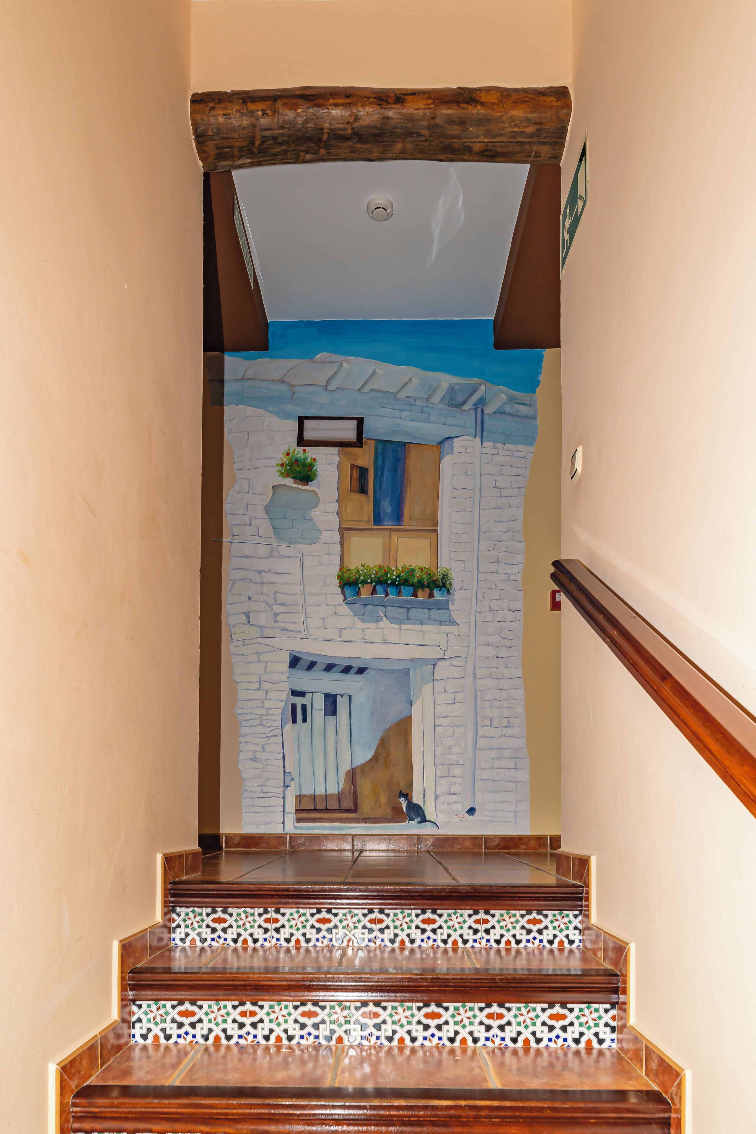 A staircase with a patterned tile design at the bottom, a stone wall mural, and a wooden handrail.