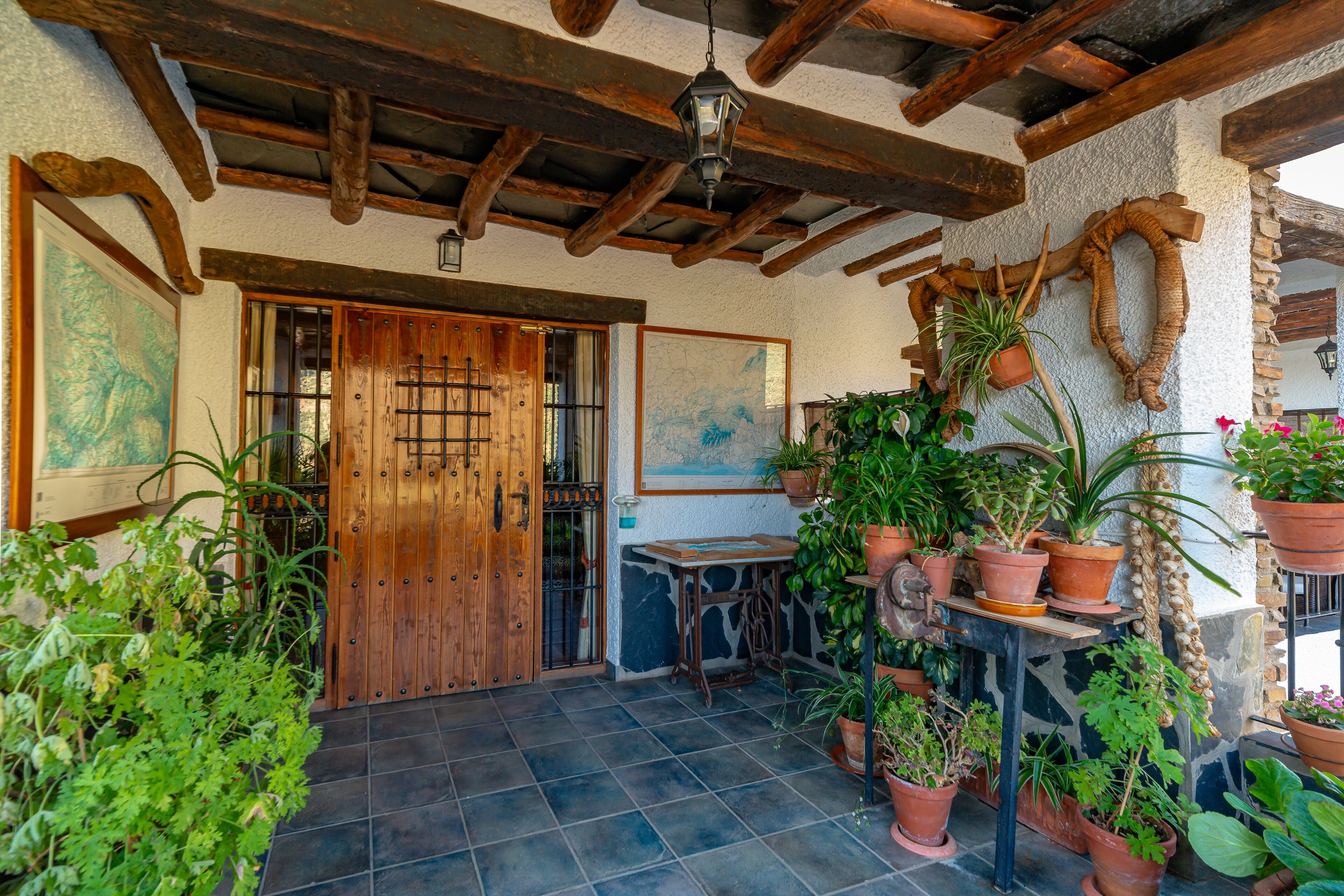 A rustic patio with wooden beams, a wooden door, and various potted plants.