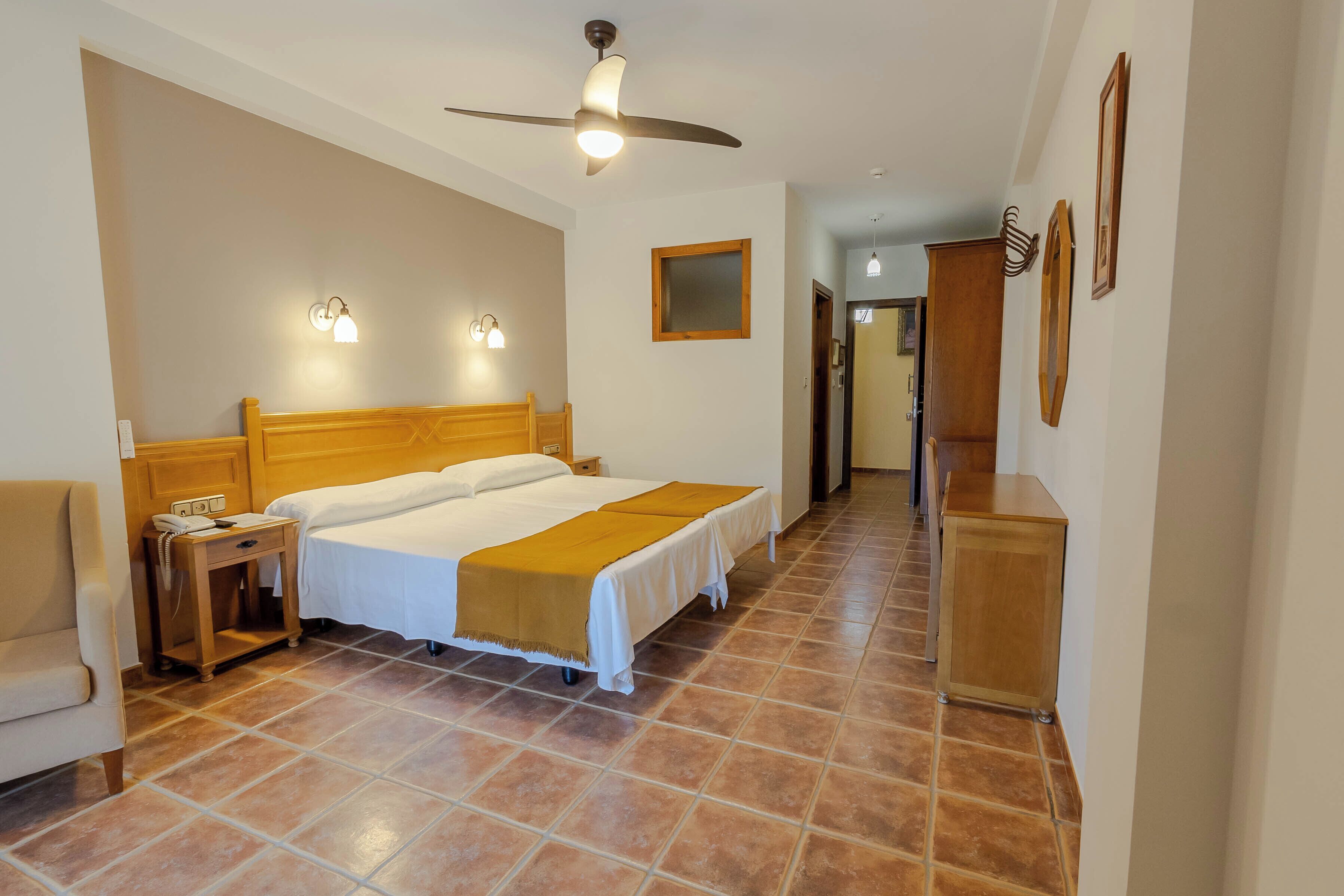A hotel room with a bed, bedside table, lamp, and a ceiling fan.