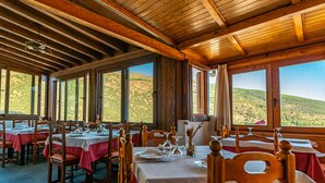 A restaurant with wooden beams and large windows overlooking a hilly landscape. Tables are set with white tablecloths and red napkins. - Hotel La Fragua II (Trevelez)