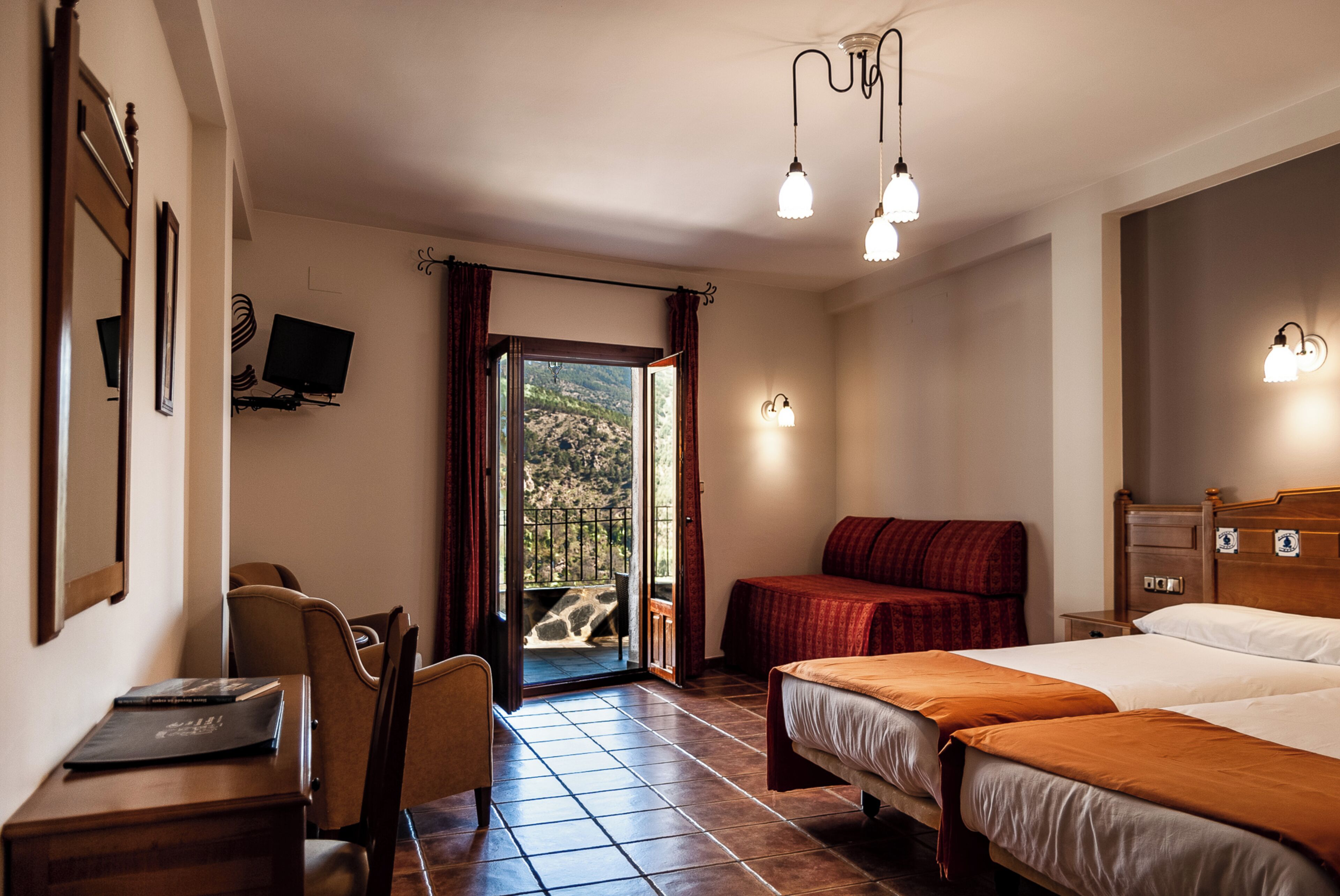 Habitación de hotel con dos camas, un escritorio con silla, televisor y balcón con vistas al exterior.