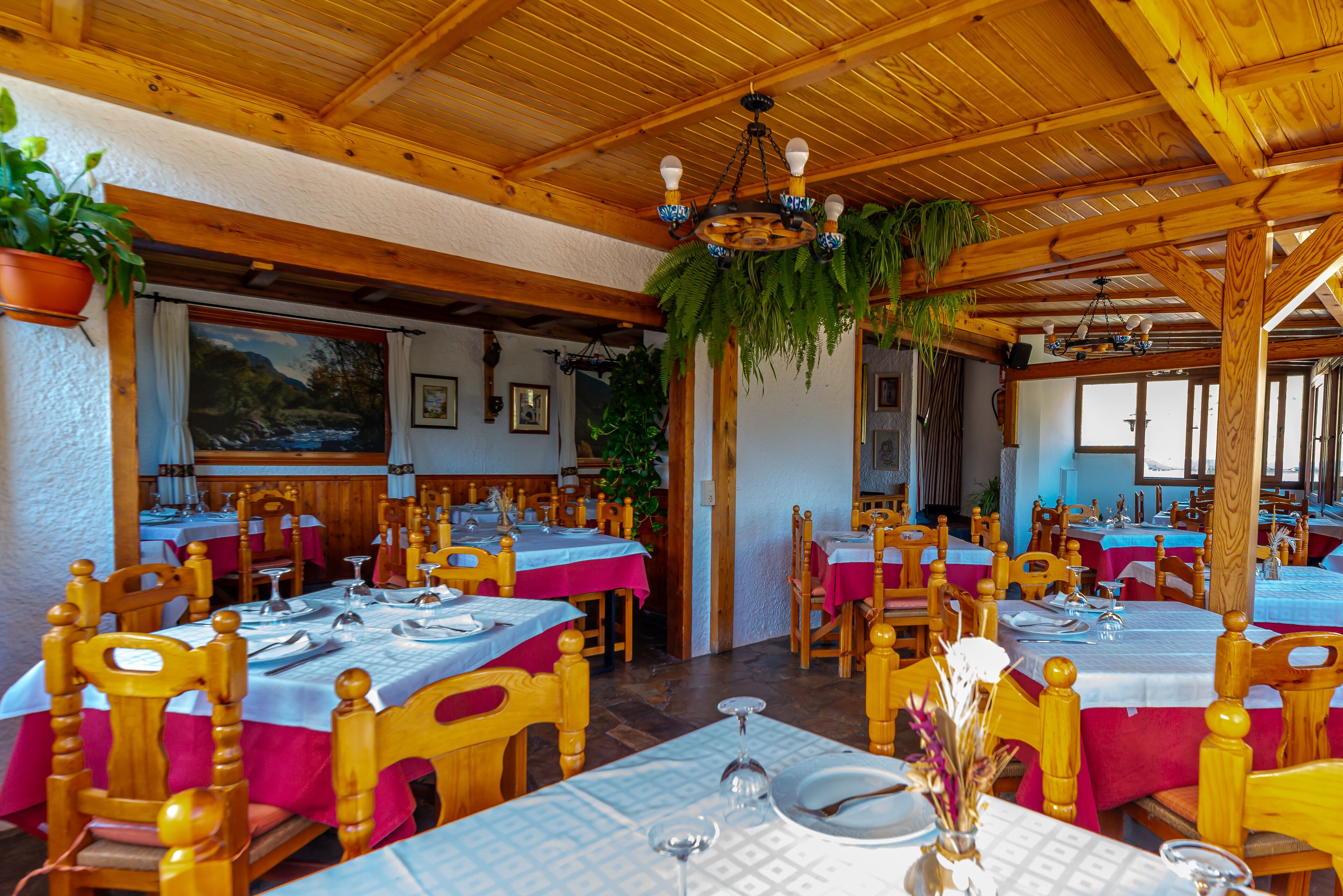 Un restaurant avec des tables et des chaises en bois, recouvertes de nappes blanches et de serviettes rouges.