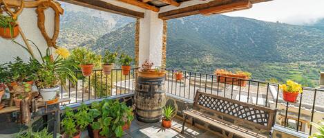 Un balcón con macetas, un banco de madera y vistas a un paisaje montañoso.