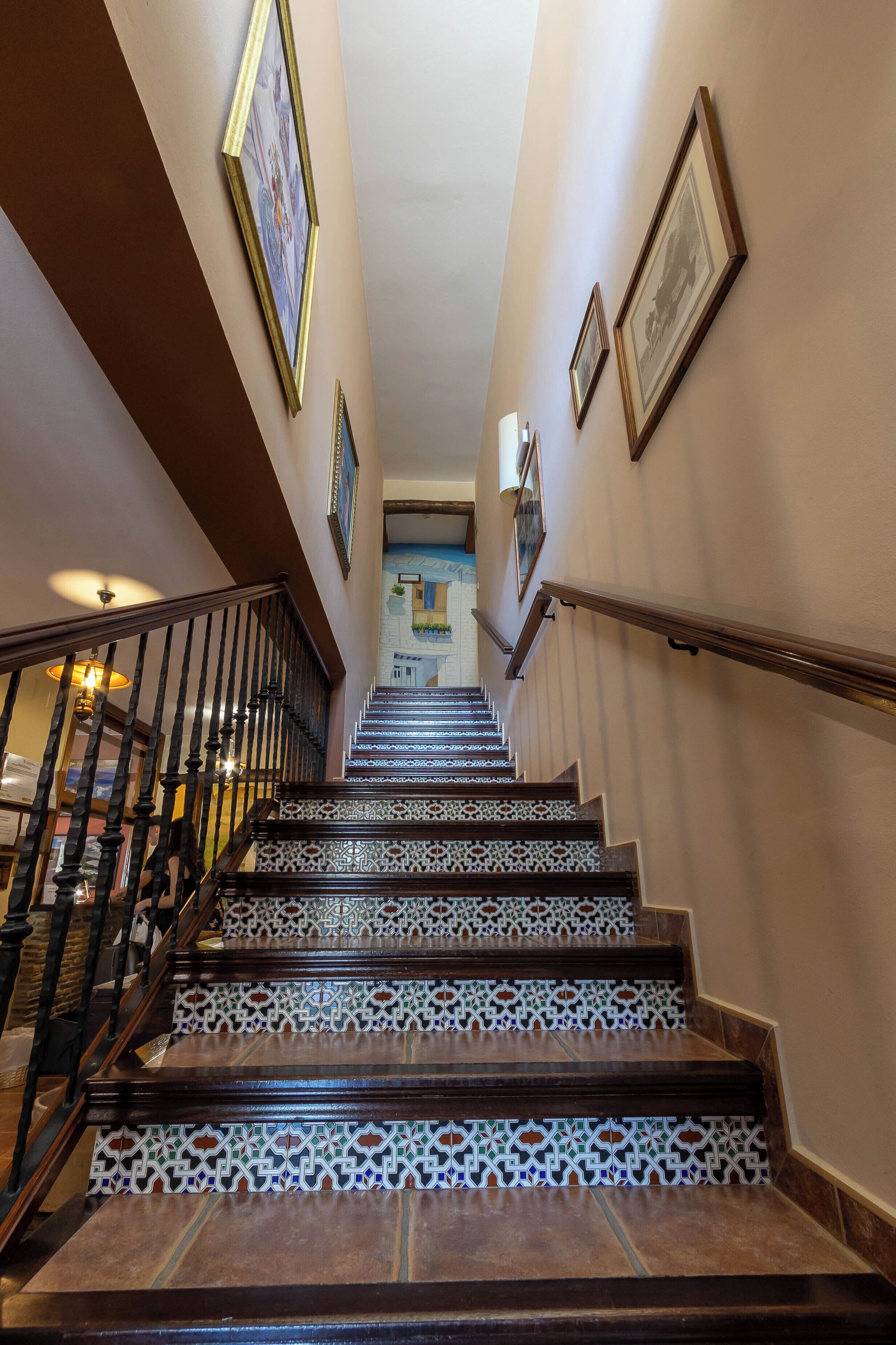 Un escalier orné de carreaux décoratifs et doté de rampes en bois, menant à une pièce d’où l’on peut admirer un bâtiment.