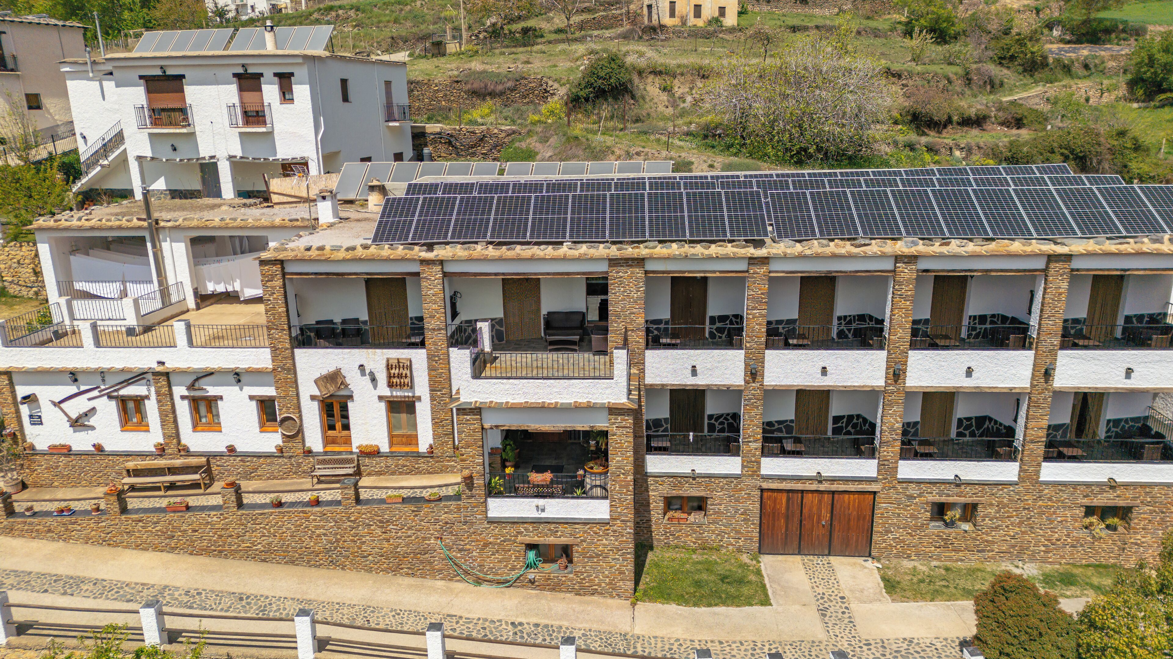 Un edificio de varios pisos con balcones, paneles solares en el techo y fachada de piedra.