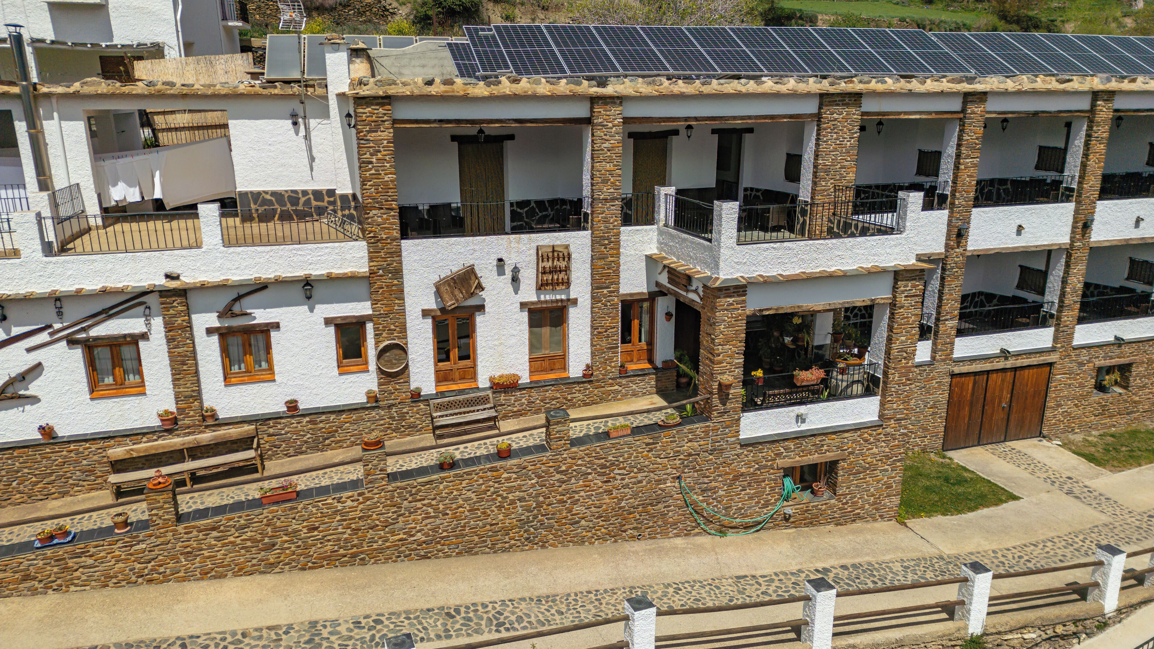 Un edificio de varios pisos con paredes de piedra y blanco, balcones y paneles solares.