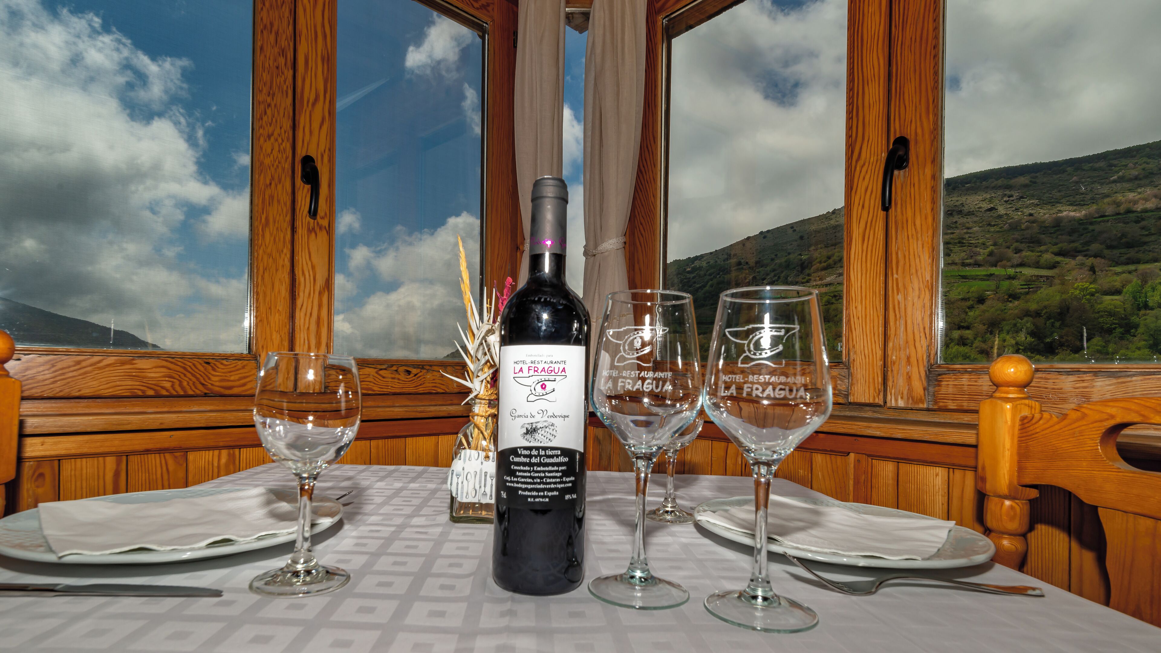Een tafel voor twee, gedekt met een fles wijn en twee wijnglazen, met een prachtig berglandschap op de achtergrond.