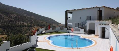 A modern building with a pool, surrounded by a well-maintained lawn and a mountainous backdrop.