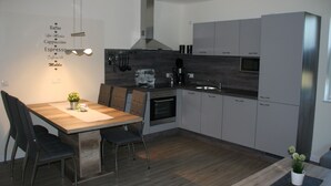 Una cocina moderna con una mesa de comedor de madera, sillas, horno empotrado y campana extractora de acero inoxidable.