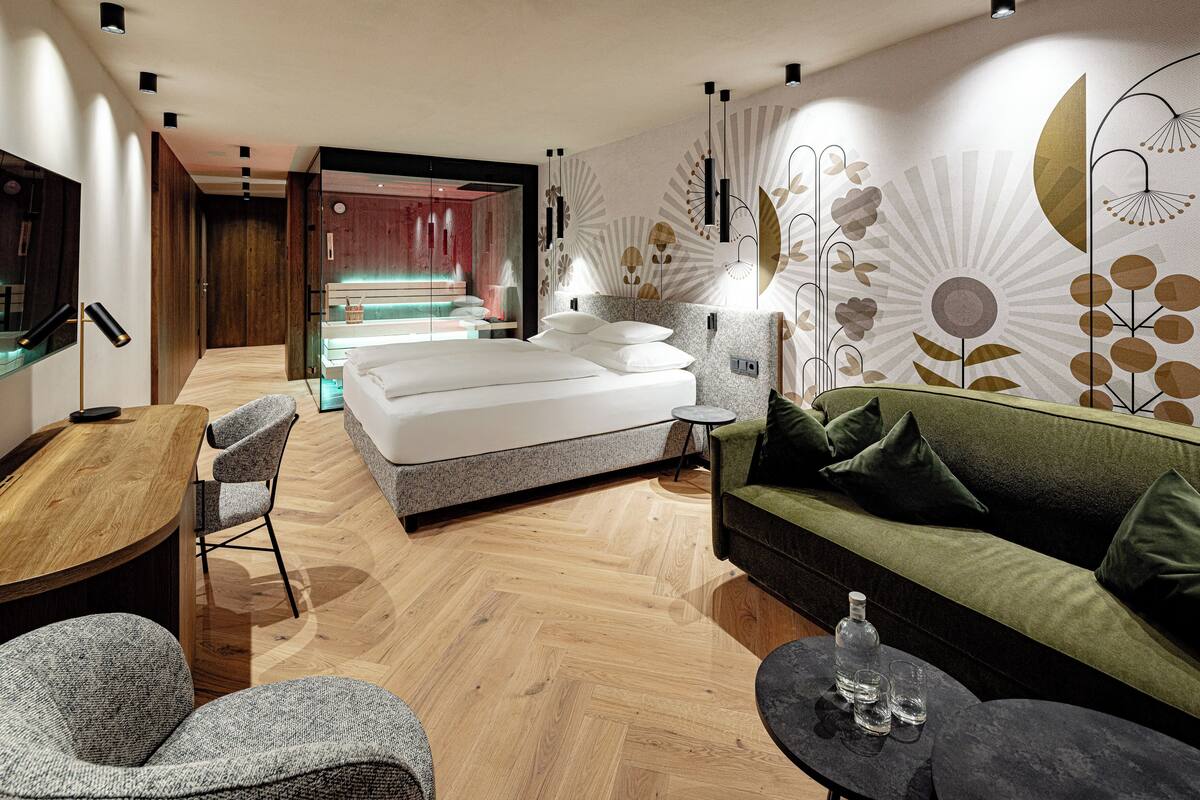 A modern hotel room with a wooden floor, a bed, a green sofa, a small round table, and a TV.