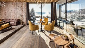 Un interior moderno con techo de madera, sofá de cuero, sillas amarillas, mesa de madera y vista a un paisaje nevado a través de amplias ventanas.