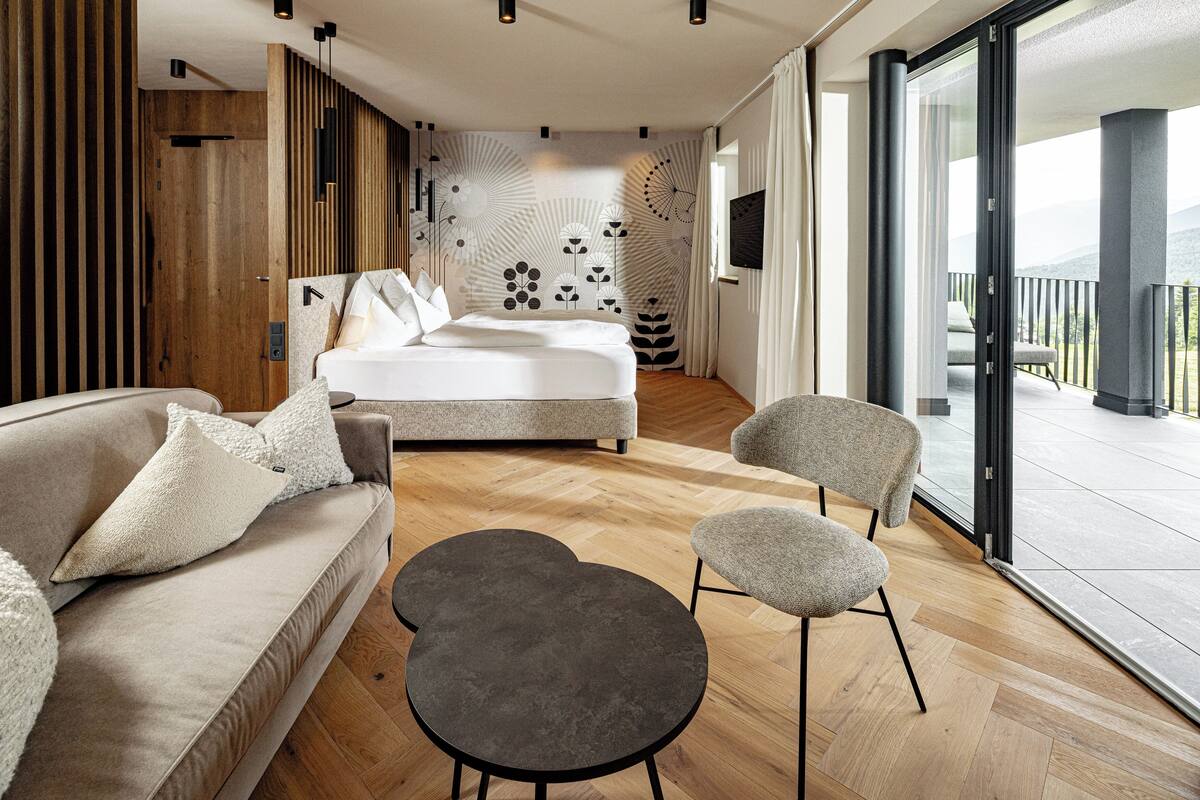 A modern bedroom with a bed, sofa, and chairs, a wooden wall, and a large window.