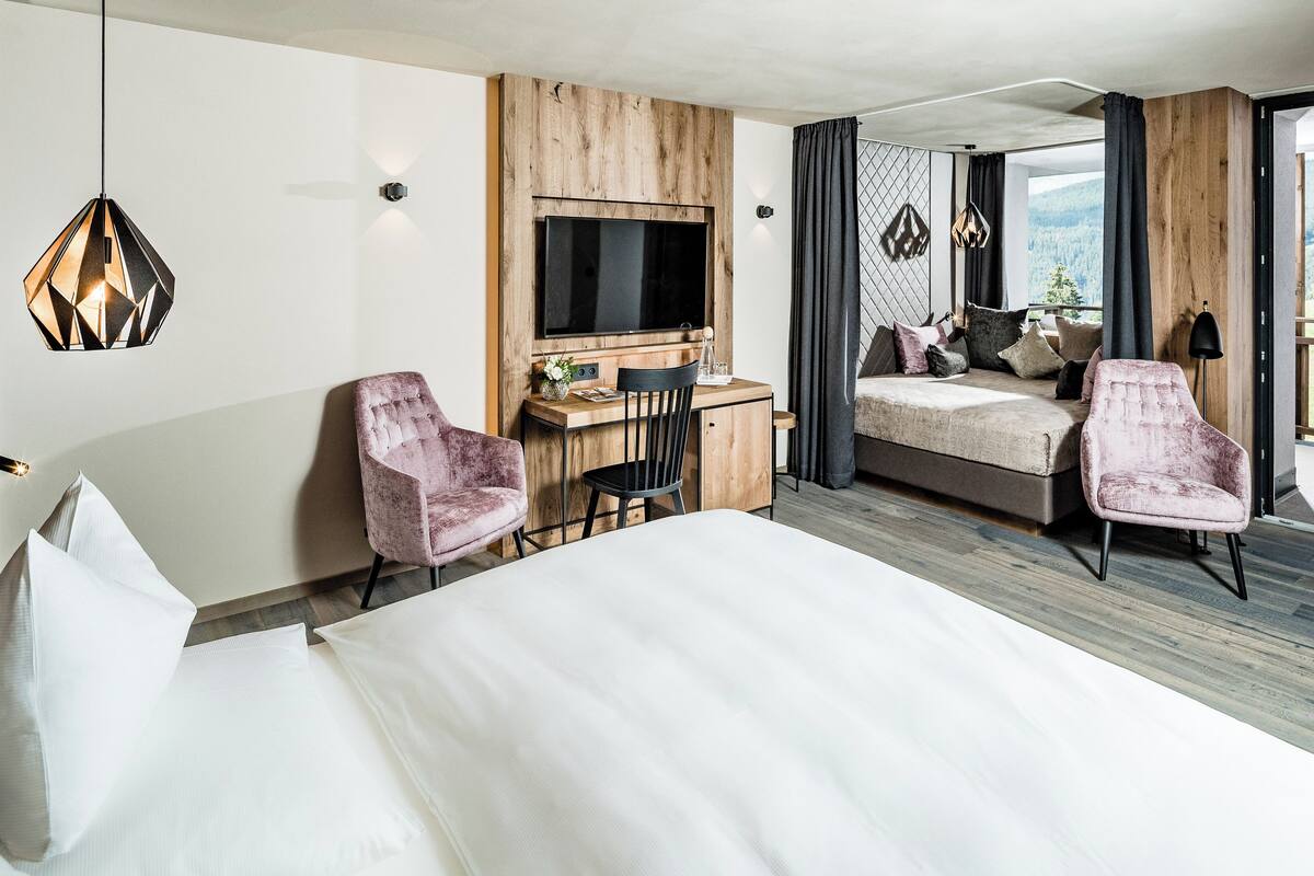 A hotel room with a bed, desk, two chairs, a TV, and a balcony with a view.