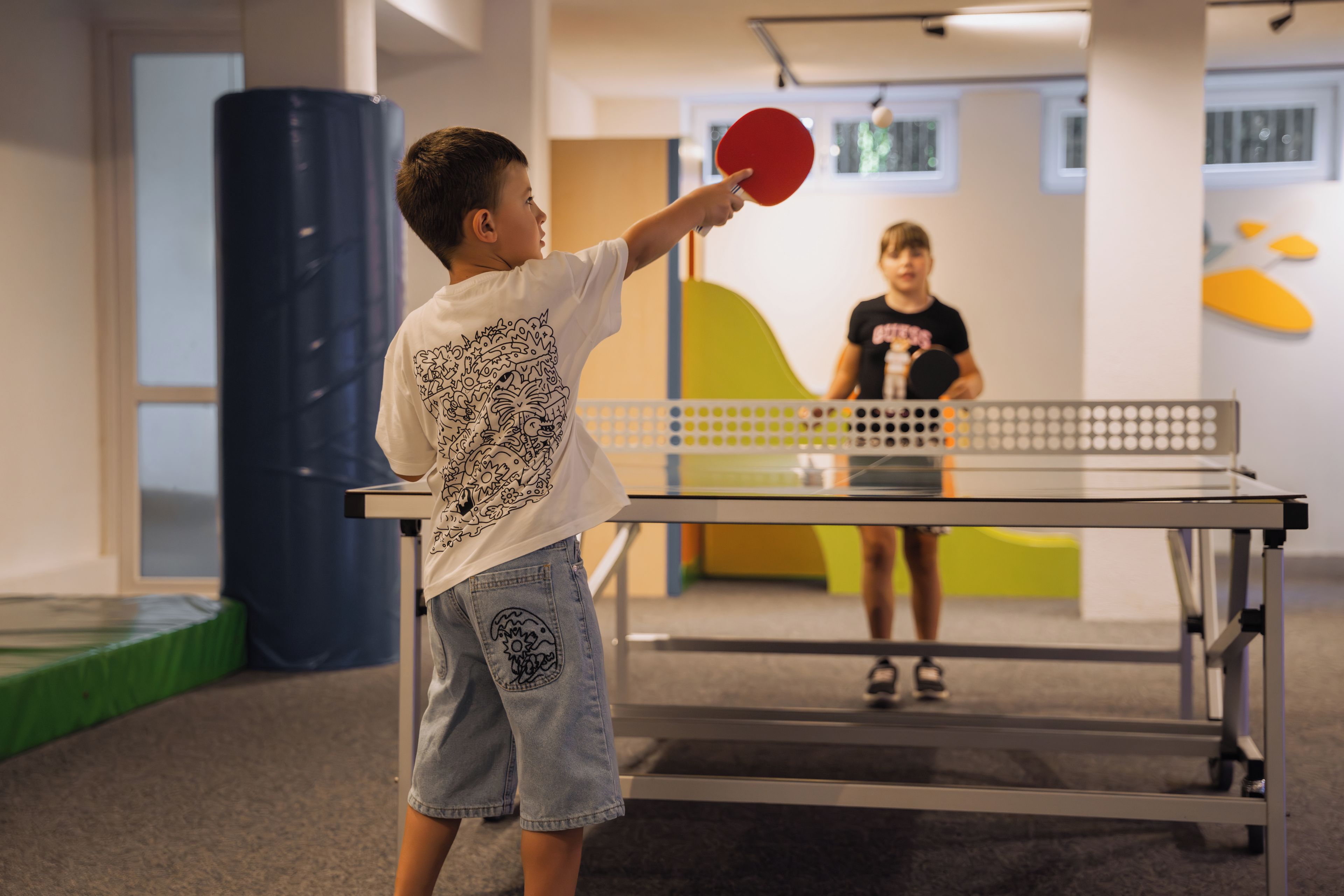 Ein Kind spielt drinnen Tischtennis mit Tisch und Netz.