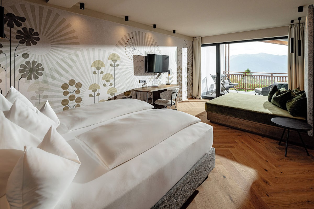 A modern hotel room with a large bed, a desk, a TV, and a balcony with a view.