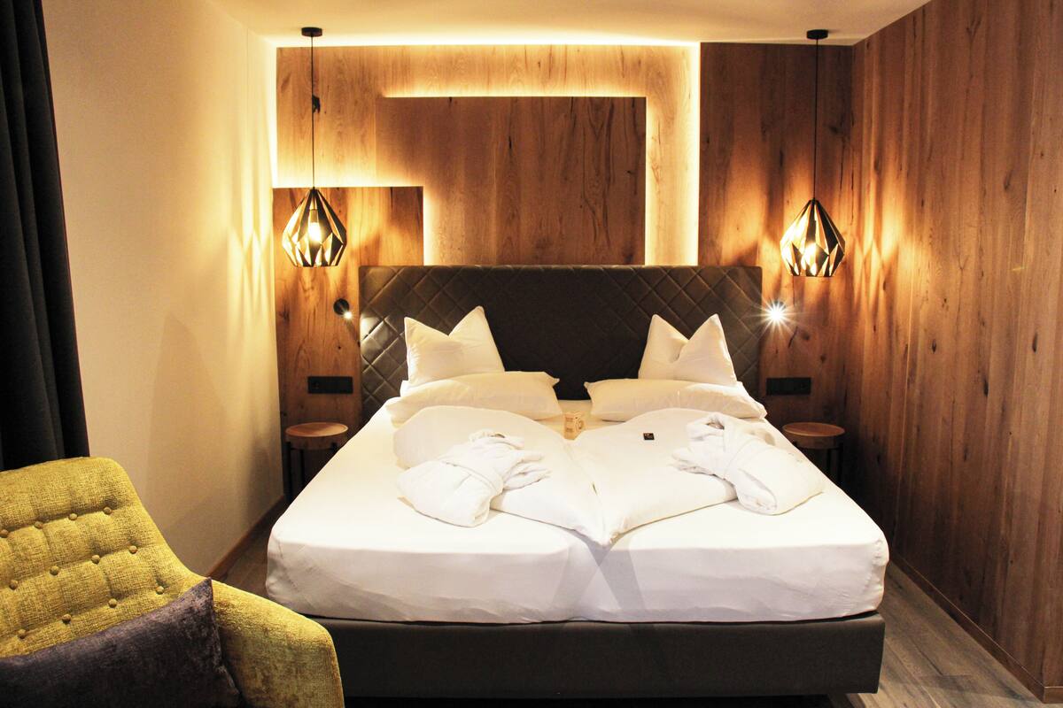 A modern hotel room with a large bed, two bedside tables, and a yellow armchair.