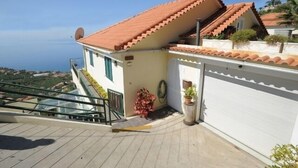 A residential property with a red-tiled roof, a balcony with a glass railing, and a view of the surrounding landscape. - 60 sqm apartment with 2 bedrooms and fantastic sea views (Arco da Calheta)