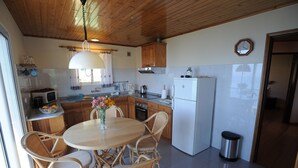 A kitchen with wooden cabinets, a dining table with chairs, a refrigerator, and a clock on the wall. - 60 sqm apartment with 2 bedrooms and fantastic sea views (Arco da Calheta)