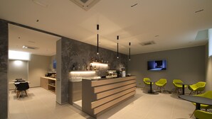 Un área de bar moderna con mostrador, asientos y una pantalla de televisión.